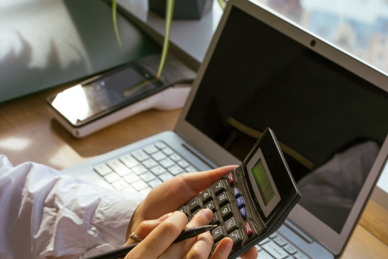 Person working out costs on a calculator in front of a laptop