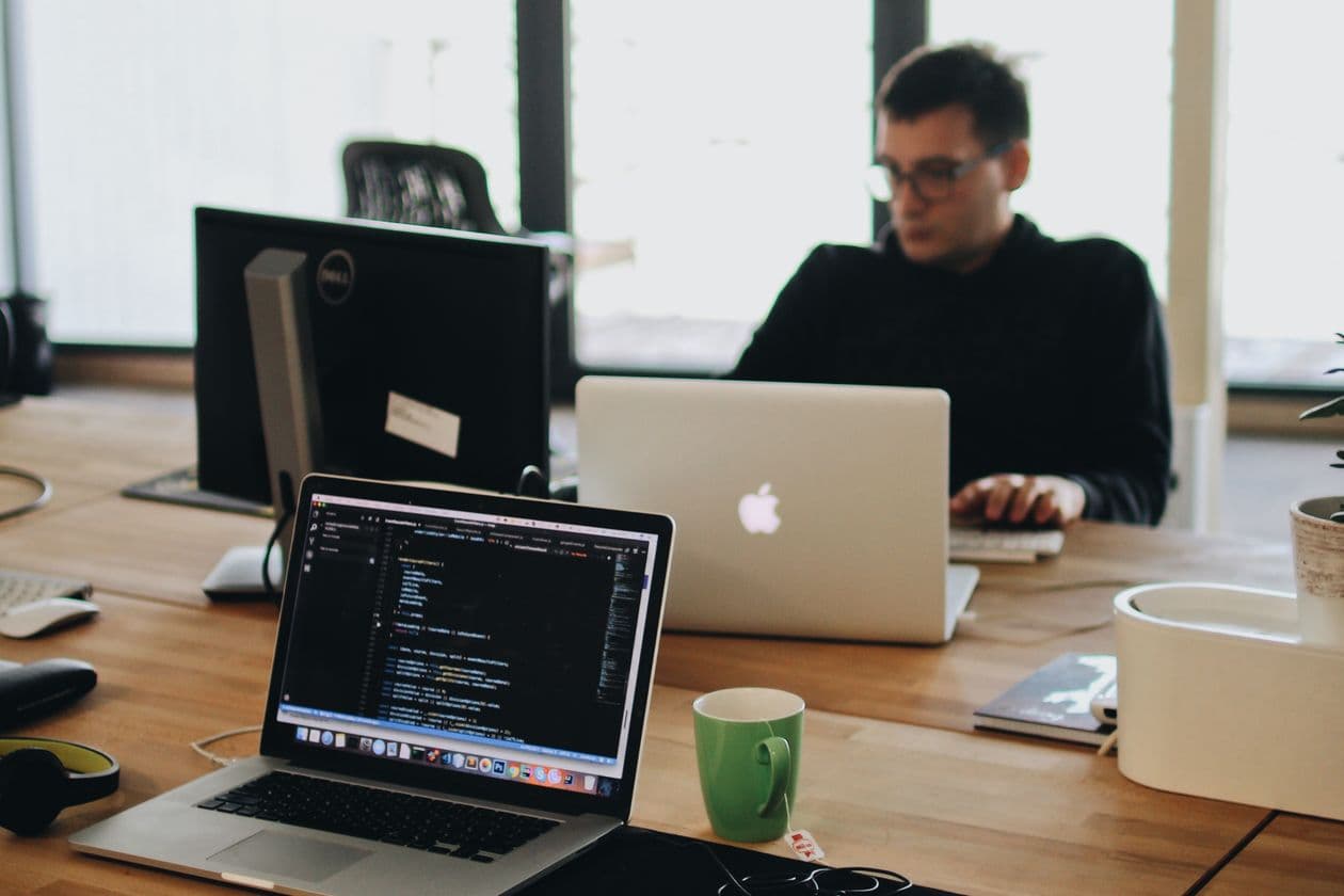Web developer working on code across a laptop and desktop monitor