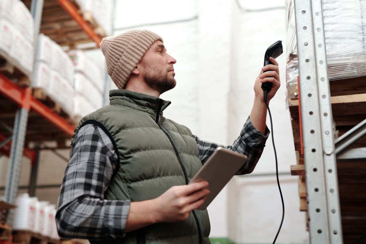Warehouse worker scanning stock with a handheld scanner and tablet between shelves