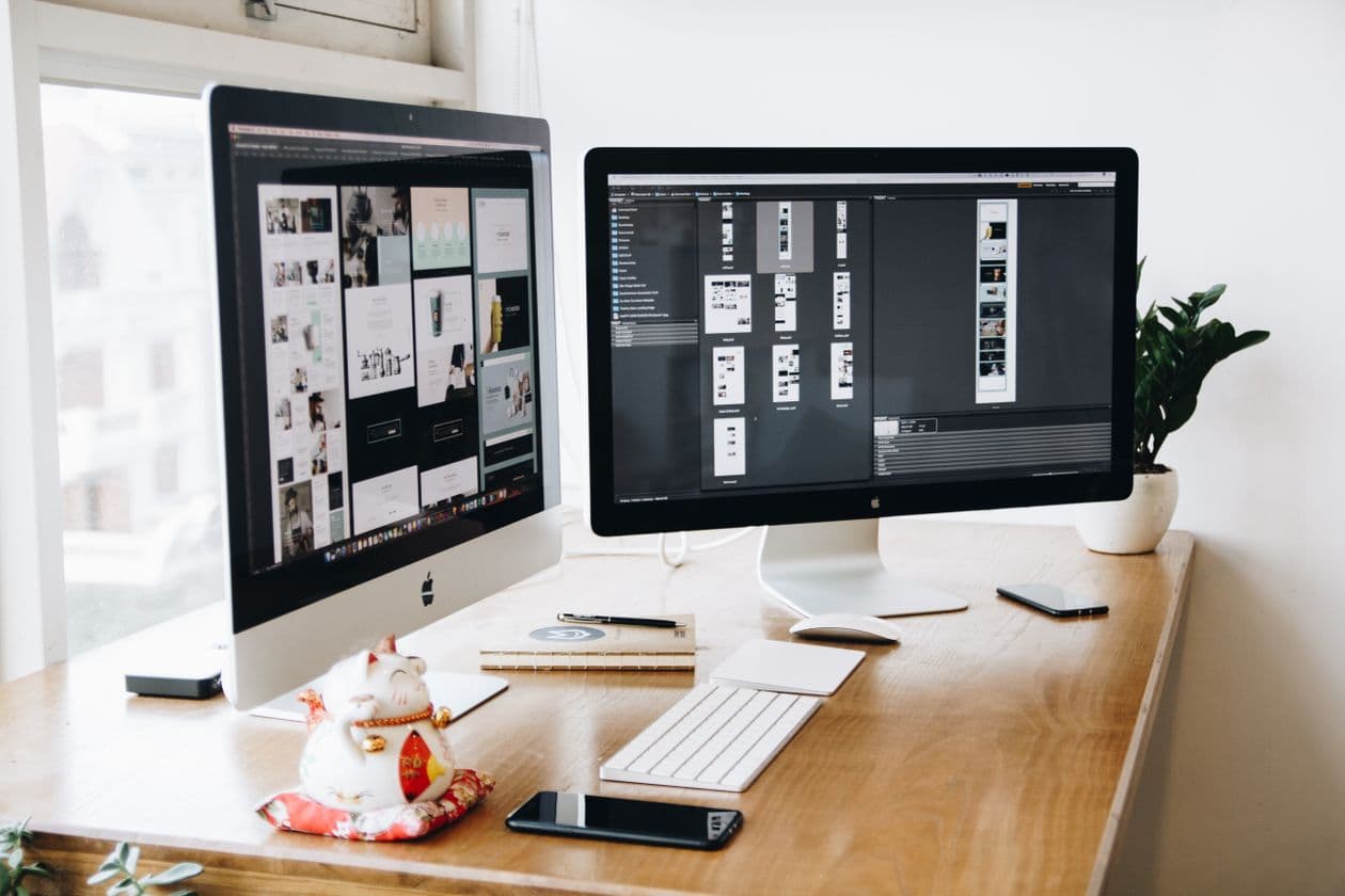 Developer workspace with two desktop monitors and smartphones on a wooden desk