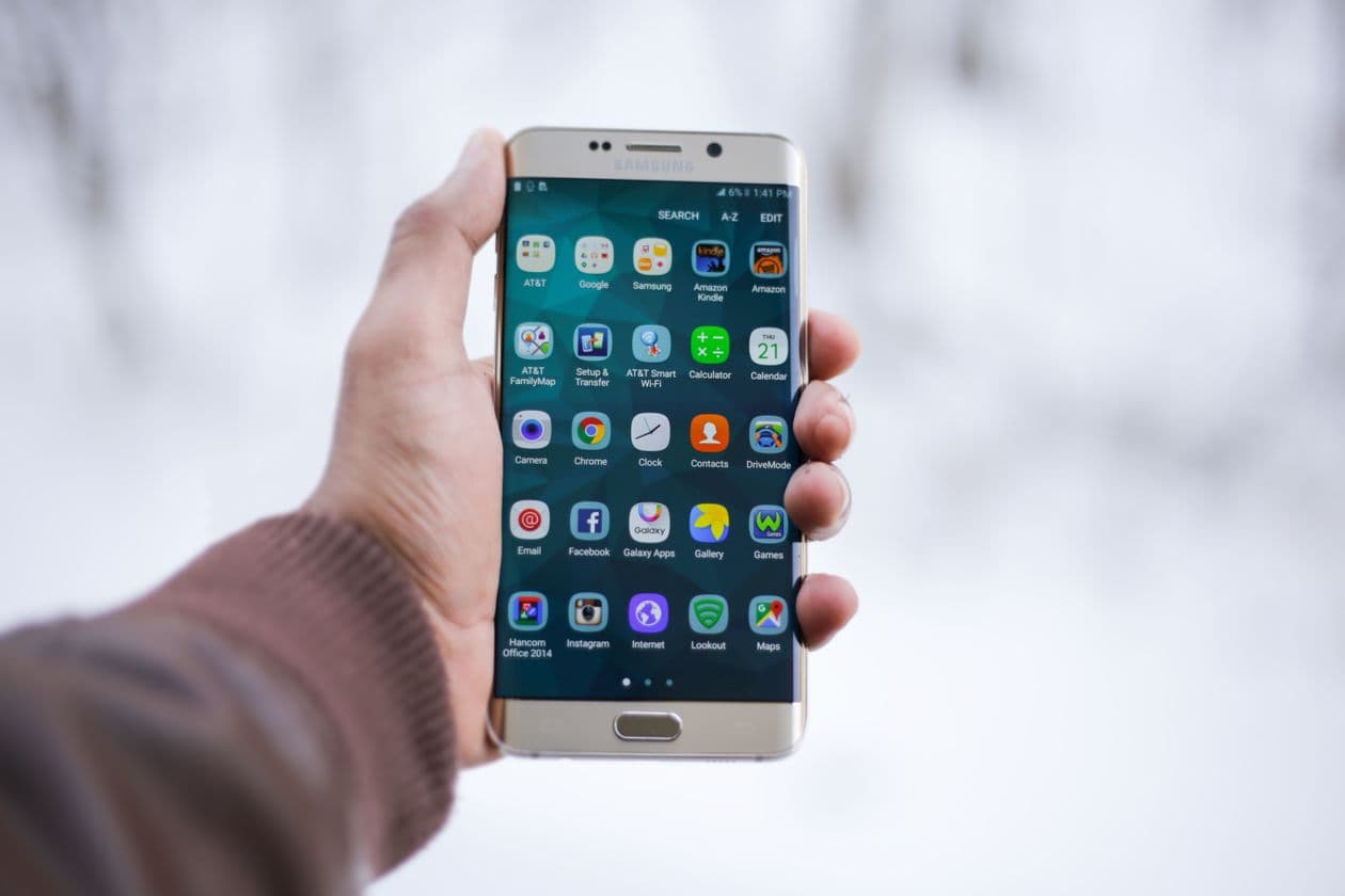 Hand holding an Android smartphone showing its home screen of app icons