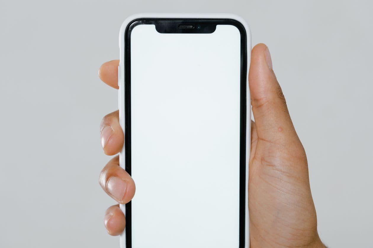 Hand holding an iPhone with a blank white screen against a grey background