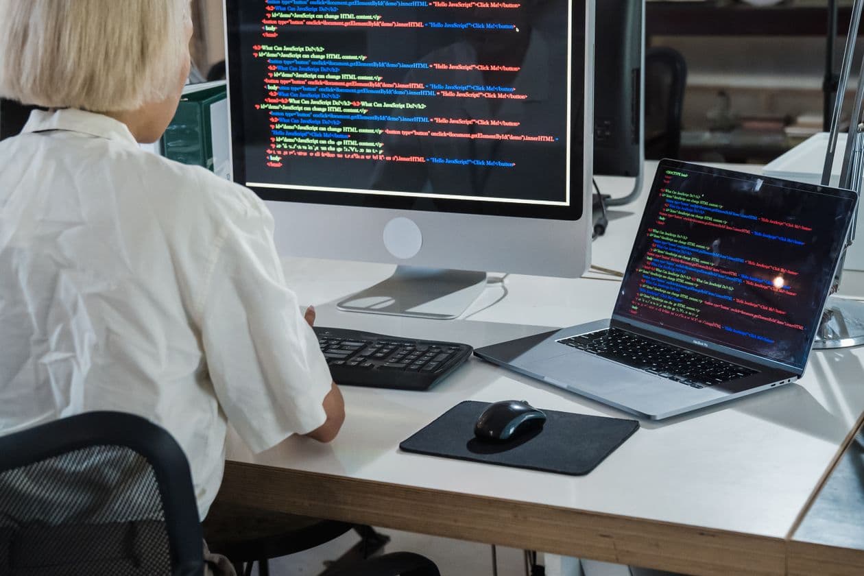 Developer working at a desk with a monitor and laptop both showing program code