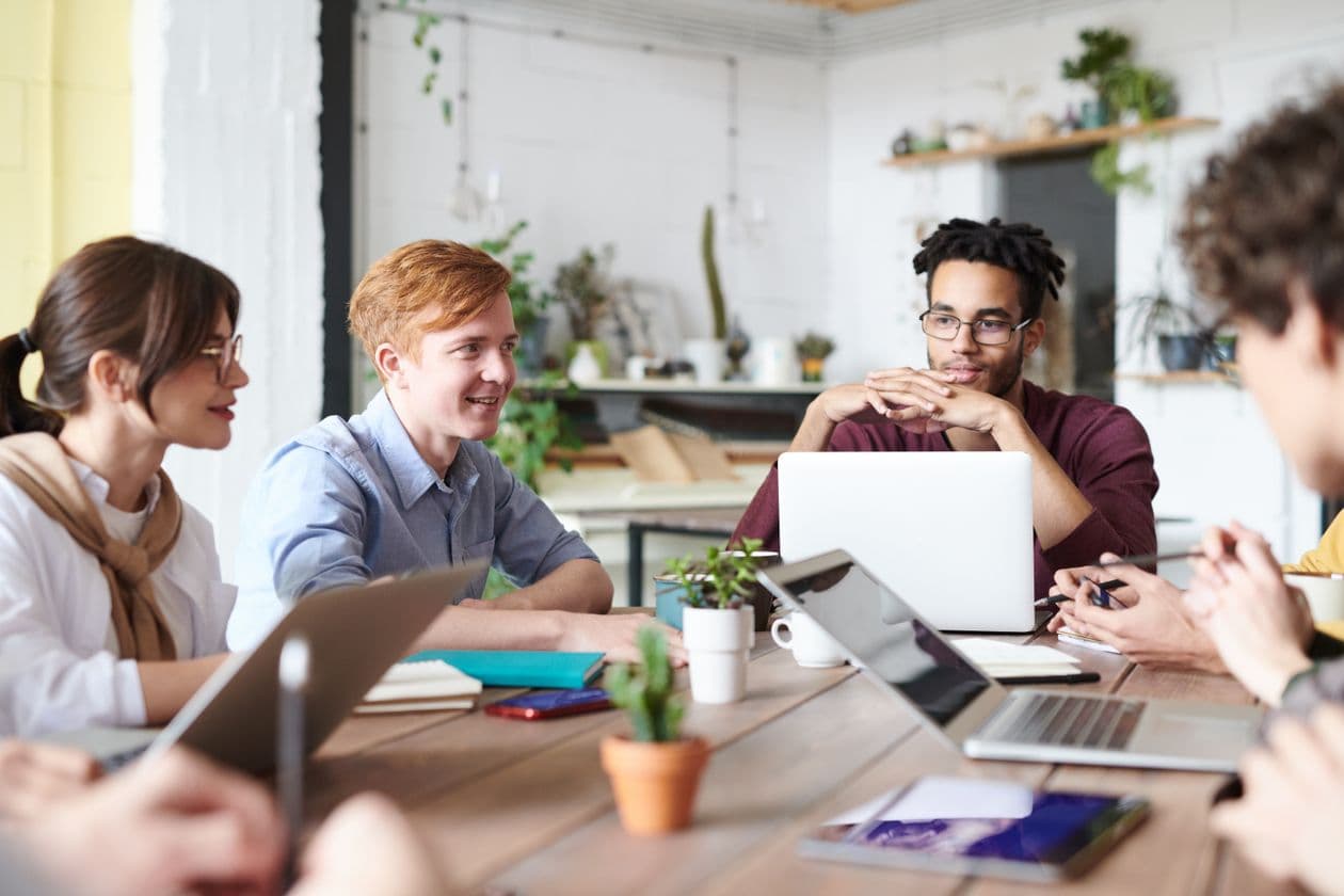 Colleagues talking around a table with laptops in a bright office