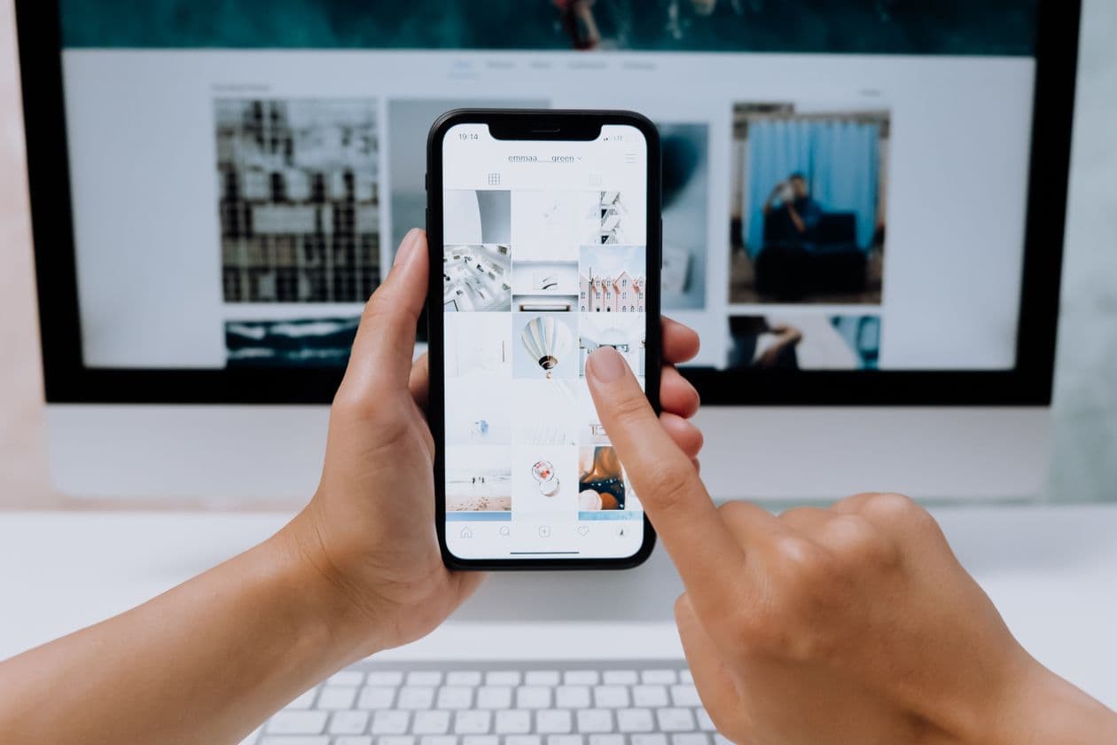 Person browsing a shopping app on a phone in front of a desktop screen