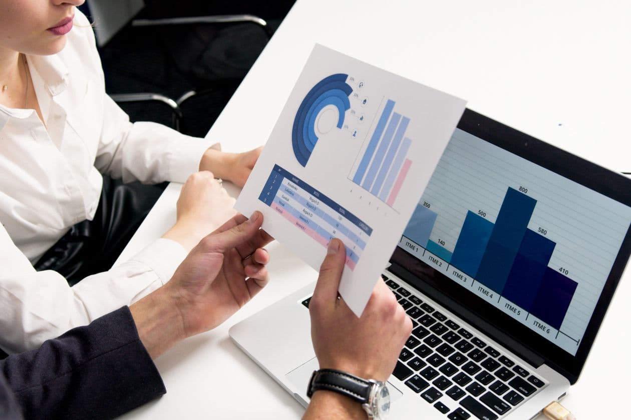 Printed business charts and a laptop showing a bar chart on a desk
