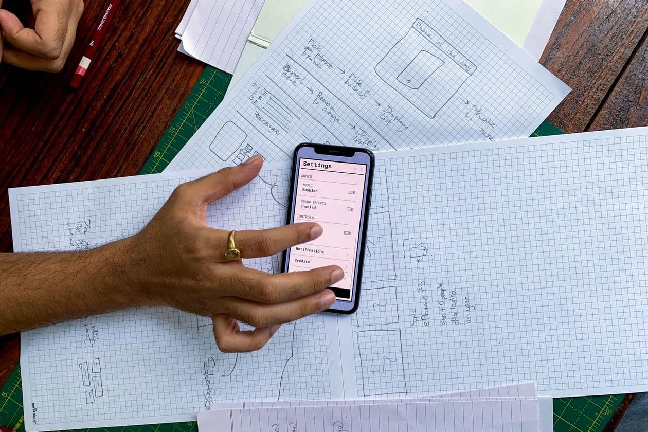 Hand holding a phone over paper sketches of app screens