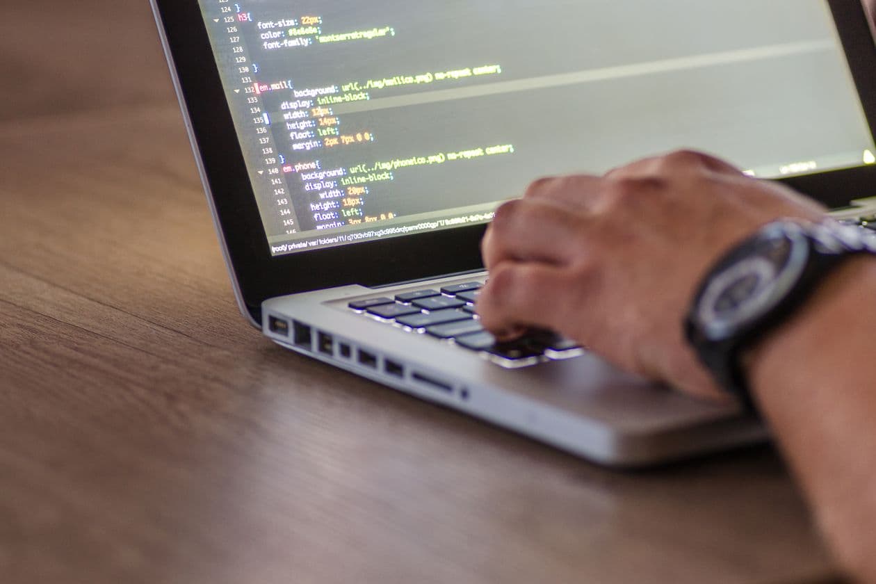 Hands typing on a laptop showing lines of code