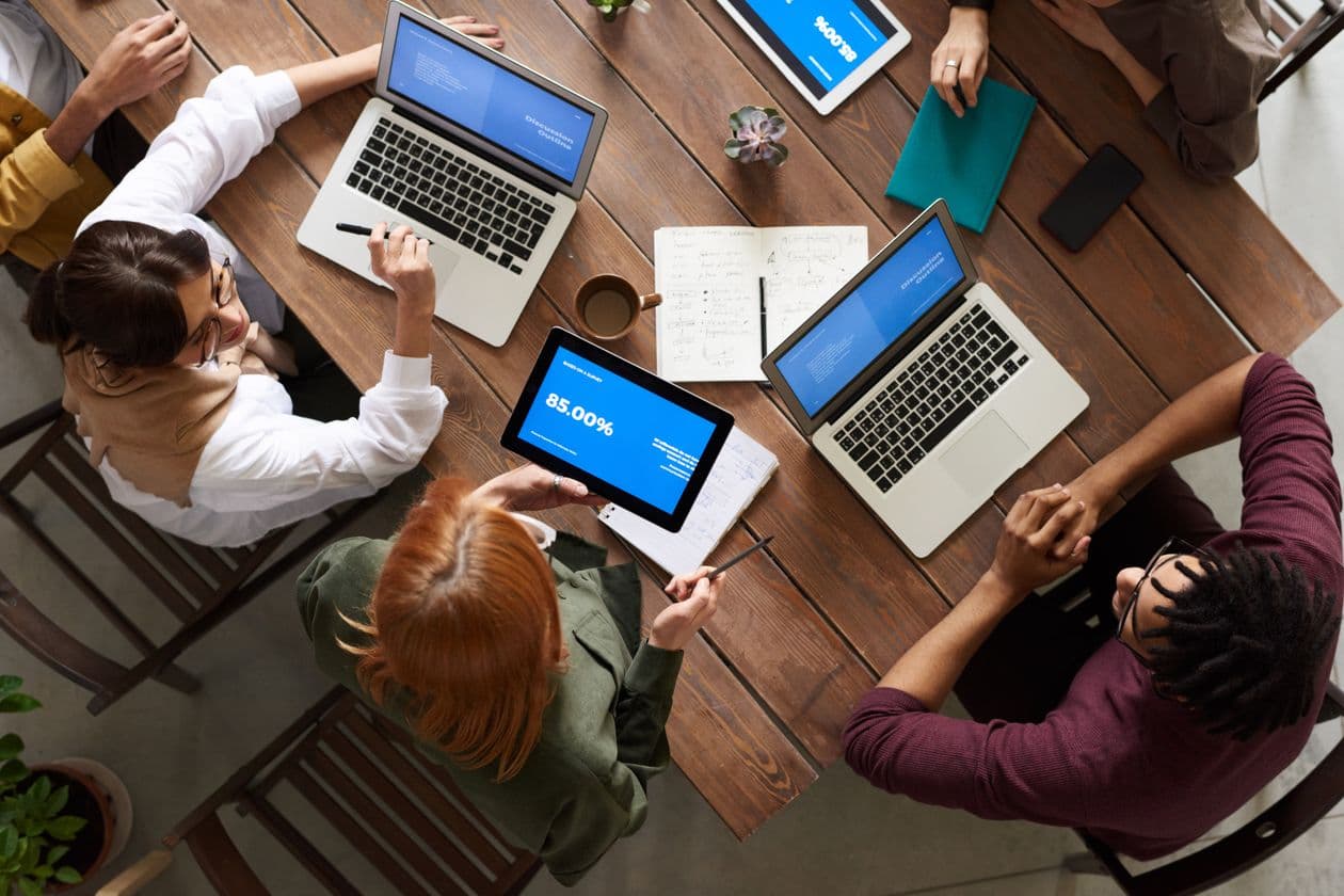 Overhead view of people working on laptops and tablets around a wooden table